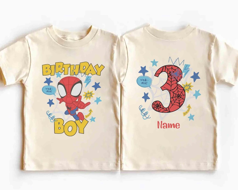 Pu&ograve; includere: Due magliette color crema. La maglietta a sinistra presenta un personaggio ragno dei cartoni animati, il testo "BIRTHDAY BOY" e stelle blu. Quella a destra mostra un grande numero "3" con motivo a ragnatela, stelle blu e il testo "Name".