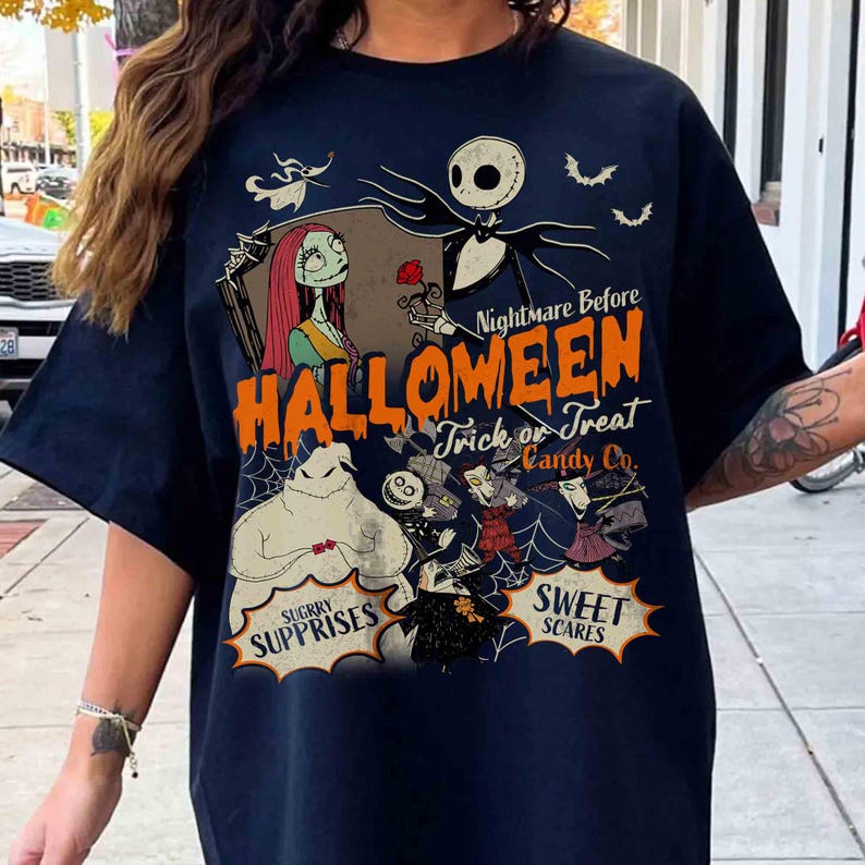 May include: A dark navy blue t-shirt featuring a graphic print of characters from The Nightmare Before Christmas. The design includes Jack Skellington, Sally, and Oogie Boogie with text that reads Nightmare Before Halloween Trick or Treat Candy Co.
