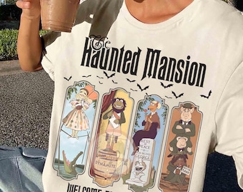 May include: A cream-colored t-shirt featuring The Haunted Mansion text and a graphic of four Muppet characters in vertical panels. Below the panels, the text reads Welcome Foolish Mortals Est. 1969. The design includes small black bats scattered above.