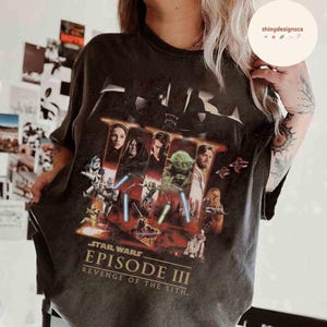 May include: Dark gray t-shirt featuring a graphic from Star Wars: Episode III - Revenge of the Sith. The design includes images of characters like Darth Vader, Yoda, and Obi-Wan Kenobi. The text "STAR WARS EPISODE III REVENGE OF THE SITH" is printed below the images.