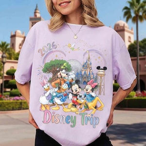 May include: A light purple t-shirt featuring a graphic print of Disney characters including Mickey Mouse, Minnie Mouse, Donald Duck, Daisy Duck, Goofy, Pluto, and Tinker Bell, with the text 2026 and Disney Trip, plus a castle and water tower.