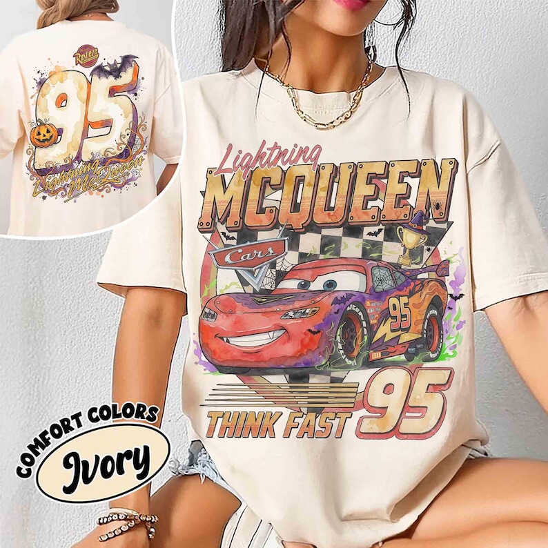 May include: An ivory short-sleeve t-shirt featuring a graphic of the red race car Lightning McQueen with the text Lightning MCQUEEN and THINK FAST 95. The design includes a checkered flag, a trophy, and Halloween-themed elements like bats.
