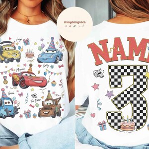 以下が含まれることがあります： 白いTシャツ。漫画の車のイラスト、カップケーキ、誕生日の装飾が描かれています。前面には、名前付きの車のキャラクターが表示されています。背面には、チェック柄の数字3と赤い文字で「NAME」と書かれています。