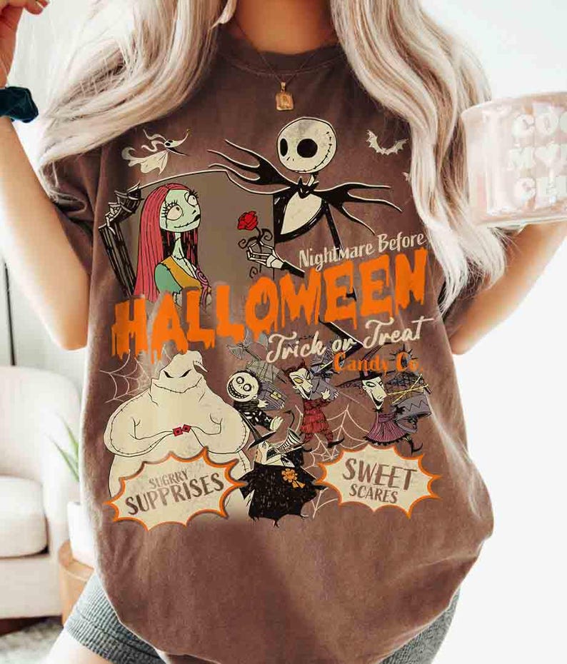 May include: A brown short-sleeve t-shirt featuring a graphic print of characters from The Nightmare Before Christmas. The design includes Jack Skellington, Sally, and Oogie Boogie with the text Nightmare Before Halloween, Trick or Treat, Candy Co.