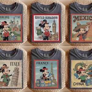 May include: Six grey t-shirts, each with a postage stamp design featuring Mickey Mouse and a different country. Countries include Germany, United Kingdom, Mexico, Italy, France, and China. The stamps have red borders and feature country names and landmarks.