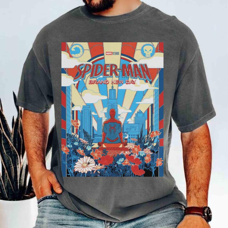 May include: A charcoal gray t-shirt featuring a graphic print of Spider-Man sitting in front of a city skyline. The design includes the text "SPIDER-MAN GRAND NEW DAY" with red, blue, and yellow colors, surrounded by a field of colorful flowers.