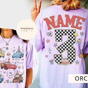 以下が含まれることがあります： Carsをテーマにした誕生日のデザインが施された、蘭色のTシャツ。前面には、漫画の車、名前、誕生日の要素が表示されています。背面には、市松模様の大きな数字3、"NAME"の文字、誕生日をテーマにしたグラフィックがあります。