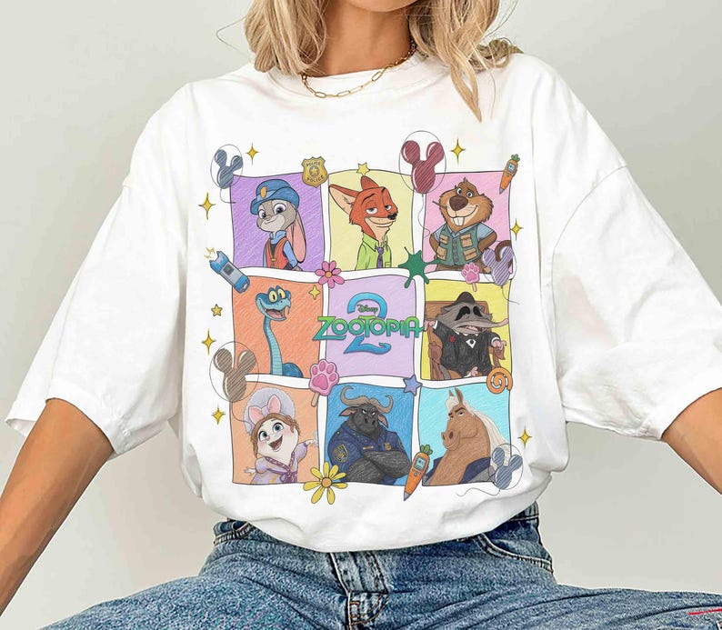 May include: White t-shirt featuring a colorful grid of Zootopia characters. The design includes Judy Hopps, Nick Wilde, and other characters from the animated film. The text "Zootopia 2" is also visible. The shirt has short sleeves.