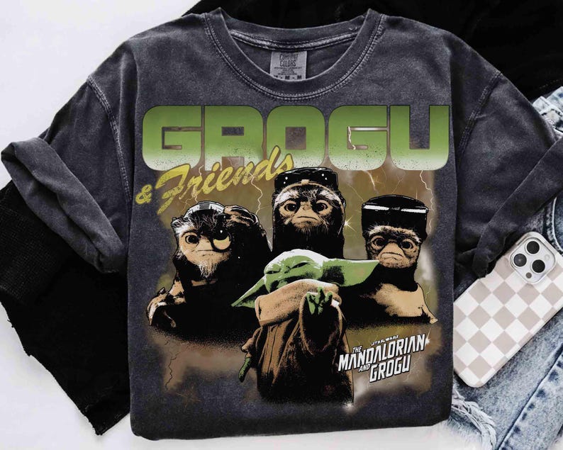 May include: Dark gray t-shirt featuring Grogu and other creatures from The Mandalorian. The shirt has the words "GROGU & Friends" in green and yellow, with a graphic of Grogu and other characters. The Star Wars logo is also visible.