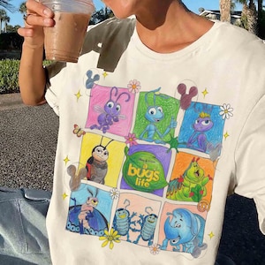 May include: Cream-coloured t-shirt with a vibrant graphic of characters from Disney Pixar's "A Bug's Life." The design presents insects in a comic strip layout, with the film's title on a green leaf.