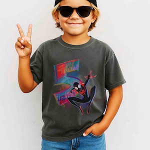 May include: Dark grey t-shirt with a colourful Spider-Man graphic and the number 5. The design includes a stylized cityscape and vibrant colour accents. The shirt is worn by a child.
