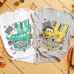 May include: Two white and gray t-shirts with a graphic design featuring a cartoon car, the number 4, and the word "SISTER". The shirts have a birthday theme with checkered flags and gift boxes.