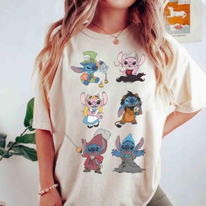 K&ouml;nnte beinhalten: Beigefarbenes T-Shirt mit farbenfrohen Cartoon-Illustrationen von Stitch-Charakteren in verschiedenen Kost&uuml;men. Die Designs zeigen Stitch als Hutmacher, K&ouml;nigin und andere Charaktere. Das Shirt ist ein l&auml;ssiger Stil.