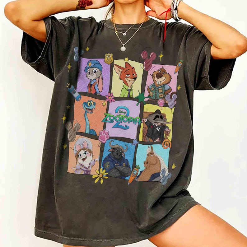 May include: Dark gray t-shirt featuring a colorful graphic of characters from the animated movie Zootopia. The design includes Judy Hopps, Nick Wilde, and other characters in a grid pattern, with the movie title prominently displayed.