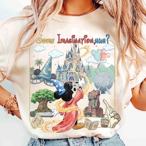 Op de afbeelding: Cr&egrave;mekleurig T-shirt met een kleurrijke afbeelding van Mickey Mouse als tovenaar, een kasteel, een tovenaars hoed en de tekst "Some Imagination, Huh?" Het ontwerp bevat andere themaparkelementen.