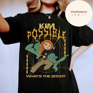 May include: Black t-shirt featuring a graphic of Kim Possible, with the text "KIM POSSIBLE" in a stylized font. The design includes Kim Possible in action, with the phrase "WHAT'S THE SITCH?" below. The shirt is a classic crew neck.