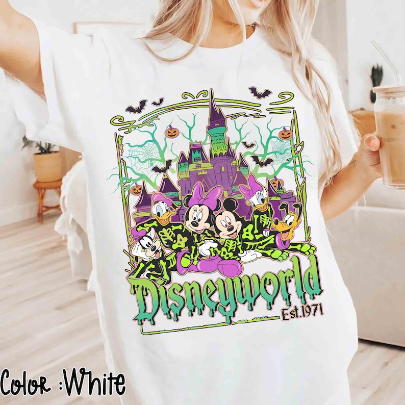 May include: White t-shirt with a Halloween design featuring Disney characters and a haunted castle. The graphic includes the words "Disneyworld" and "Est.1971" in green and black.