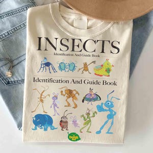 May include: Cream-colored t-shirt featuring the word "INSECTS" above the text "Identification And Guide Book." Below are colorful cartoon illustrations of various insects. The shirt also has the "bug's life" logo.
