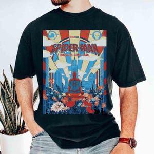 May include: A black t-shirt featuring a graphic print of Spider-Man sitting on a rooftop overlooking a city skyline. The design includes the text 'SPIDER-MAN BRAND NEW DAY' in red and blue, surrounded by colorful flowers and a sunburst background.