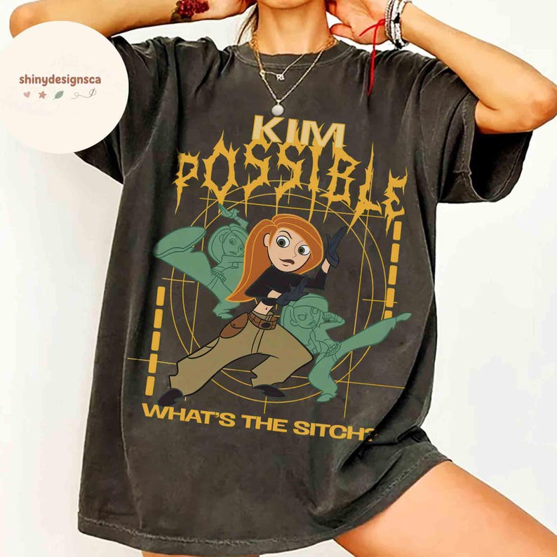 May include: Dark gray t-shirt featuring a graphic of Kim Possible with the text "KIM POSSIBLE" in yellow and the phrase "WHAT'S THE SITCH" in white. The design includes a cartoon image of Kim Possible in action.