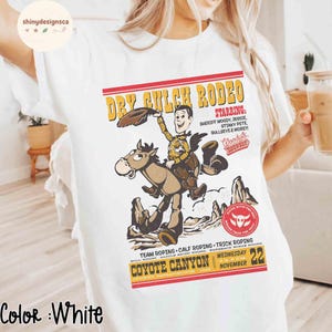 Puede incluir: Camiseta blanca con un dise&ntilde;o tem&aacute;tico de rodeo. El dise&ntilde;o incluye el texto "Dry Gulch Rodeo" con un vaquero de dibujos animados montando a caballo. Texto adicional incluye "Coyote Canyon" y "Mi&eacute;rcoles 22 de noviembre".