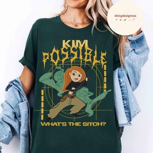 May include: Dark green t-shirt featuring a graphic of Kim Possible with the text "KIM POSSIBLE" in gold lettering. The phrase "WHAT'S THE SITCH?" is printed below the graphic. The design includes a cartoon image of Kim Possible and two other characters.
