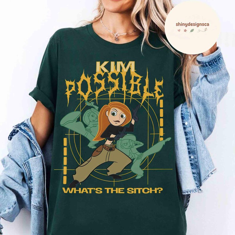 May include: Dark green t-shirt featuring a graphic of Kim Possible with the text "KIM POSSIBLE" in gold lettering. The phrase "WHAT'S THE SITCH?" is printed below the graphic. The design includes a cartoon image of Kim Possible and two other characters.