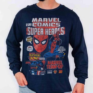 May include: A navy blue long-sleeve shirt featuring a vintage-style Marvel Comics graphic print. The design includes Spider-Man, Iron Man, Black Panther, Black Widow, and Captain America with text reading Marvel Comics Super Heroes and Marvel Team-Up.