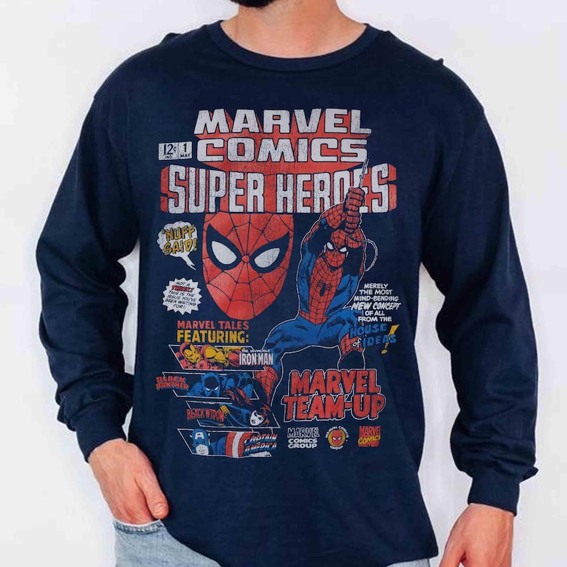 May include: A navy blue long-sleeve shirt featuring a vintage-style Marvel Comics graphic print. The design includes Spider-Man, Iron Man, Black Panther, Black Widow, and Captain America with text reading Marvel Comics Super Heroes and Marvel Team-Up.