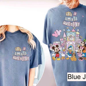Pu&ograve; includere: T-shirt blu jeans con la scritta "it's a small world!" sul davanti e sul retro. Il retro presenta una grafica colorata di personaggi Disney e un castello.