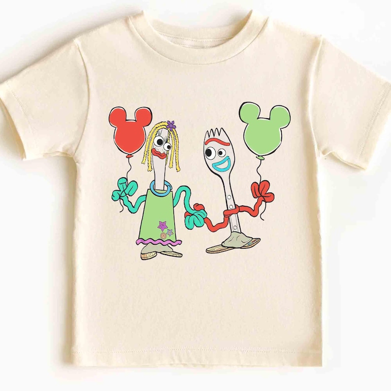 May include: Cream-colored t-shirt featuring a cartoon illustration of two fork-shaped characters holding Mickey Mouse-shaped balloons. One balloon is red, the other is green. The characters are in green and purple outfits.