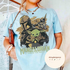 Puede incluir: Camiseta azul claro con un dise&ntilde;o de The Mandalorian y Grogu, con una nave espacial. El texto "MANDALORIAN - THIS IS THE WAY" est&aacute; impreso debajo. La camiseta tiene un corte holgado.