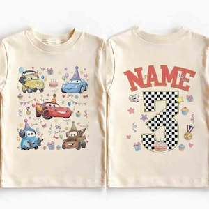 以下が含まれることがあります： クリーム色の幼児用Tシャツ。カラフルな漫画の車のグラフィックと誕生日の要素が特徴です。 シャツの背面には、市松模様の数字「3」と、その上に「NAME」という文字が表示されています。