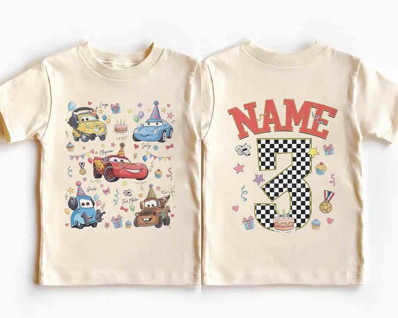 以下が含まれることがあります： クリーム色の幼児用Tシャツ。カラフルな漫画の車のグラフィックと誕生日の要素が特徴です。 シャツの背面には、市松模様の数字「3」と、その上に「NAME」という文字が表示されています。