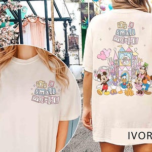 Pu&ograve; includere: T-shirt color avorio con la scritta "it's a small world!" sul davanti e sul retro. Il retro presenta una grafica colorata di un castello e dei personaggi Disney, tra cui Topolino, Paperino e Pippo.