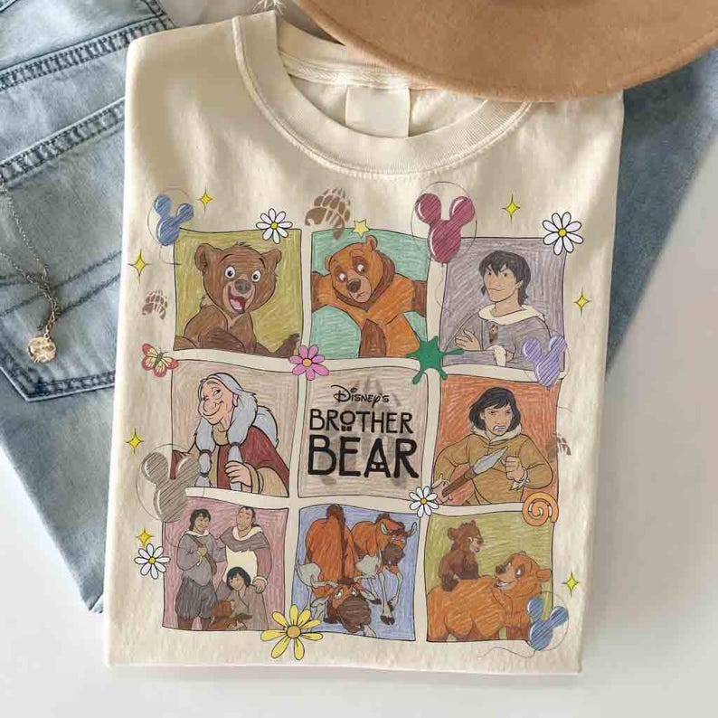 K&ouml;nnte beinhalten: Cremefarbenes T-Shirt mit einer farbenfrohen Grafik von Charakteren aus Disneys "B&auml;renbr&uuml;der". Das Design umfasst Bilder von B&auml;ren, Menschen und den Filmtitel. Das Shirt ist auf einer Denim-Oberfl&auml;che gefaltet.