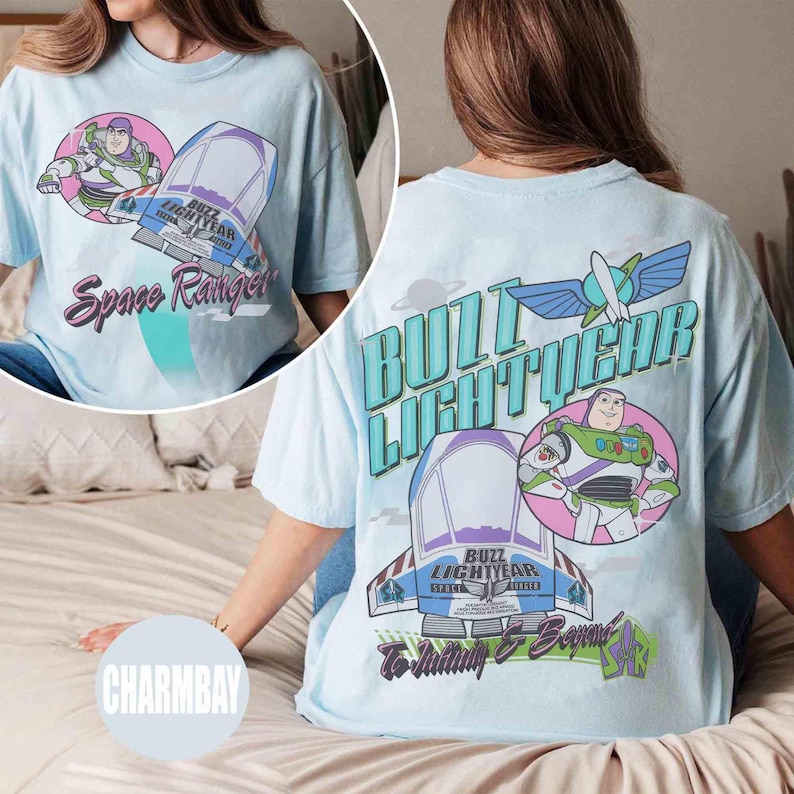 May include: A light blue t-shirt featuring Buzz Lightyear graphics. The back displays the text "BUZZ LIGHTYEAR" in large teal letters, a Buzz Lightyear character illustration, a spaceship, and the text "To Infinity & Beyond" in a script font.