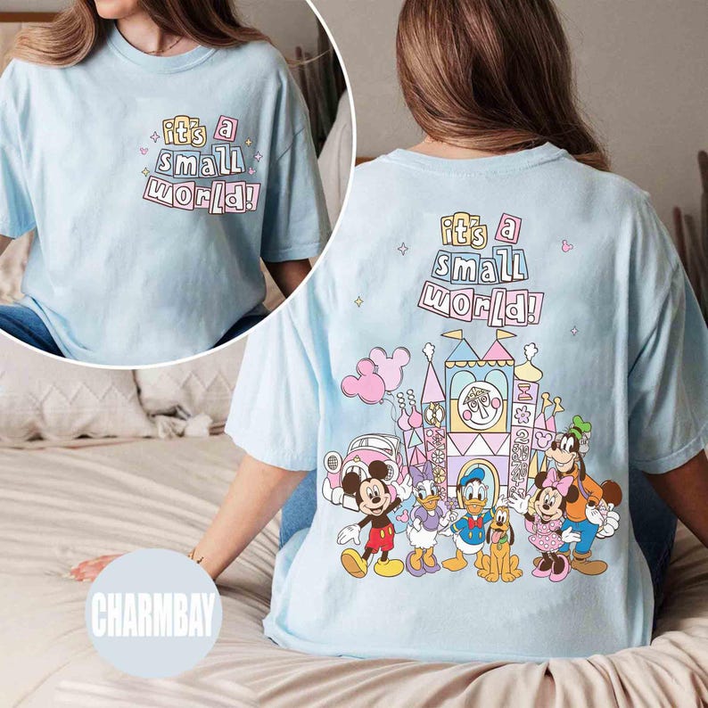 Pu&ograve; includere: T-shirt azzurra con la scritta "It's a Small World!" sul davanti e sul retro. Il retro presenta una grafica colorata di personaggi Disney e un castello. Stile casual e confortevole.