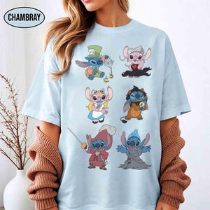 K&ouml;nnte beinhalten: Hellblaues T-Shirt mit dem Cartoon-Charakter Stitch in verschiedenen Kost&uuml;men. Das T-Shirt hat einen Rundhalsausschnitt und kurze &Auml;rmel. Der Markenname "CHAMBRAY" ist oben links aufgedruckt.