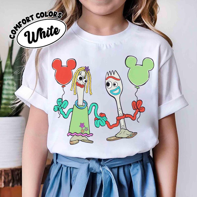 May include: White t-shirt with a cartoon graphic of two utensil characters holding Mickey Mouse-shaped balloons. One character wears a green dress. The text "COMFORT COLORS White" is in a white oval on the top left.