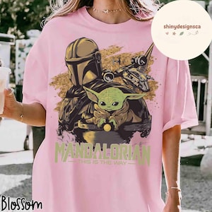 Puede incluir: Camiseta rosa claro con un dise&ntilde;o de The Mandalorian y Grogu, en tonos dorados y marrones. El texto "MANDALORIAN" y "THIS IS THE WAY" est&aacute; impreso en verde. La camiseta tiene un corte holgado.