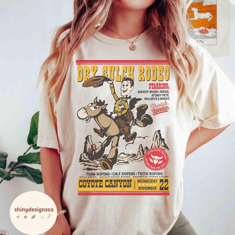 Puede incluir: Camiseta color crema con un gr&aacute;fico de estilo vintage para el "Dry Gulch Rodeo". El dise&ntilde;o incluye un vaquero de dibujos animados montando a caballo, con texto que dice "Starring Sheriff Woody, Jessie, Stinky Pete, Bullseye & More!!!" y "Coyote Canyon."