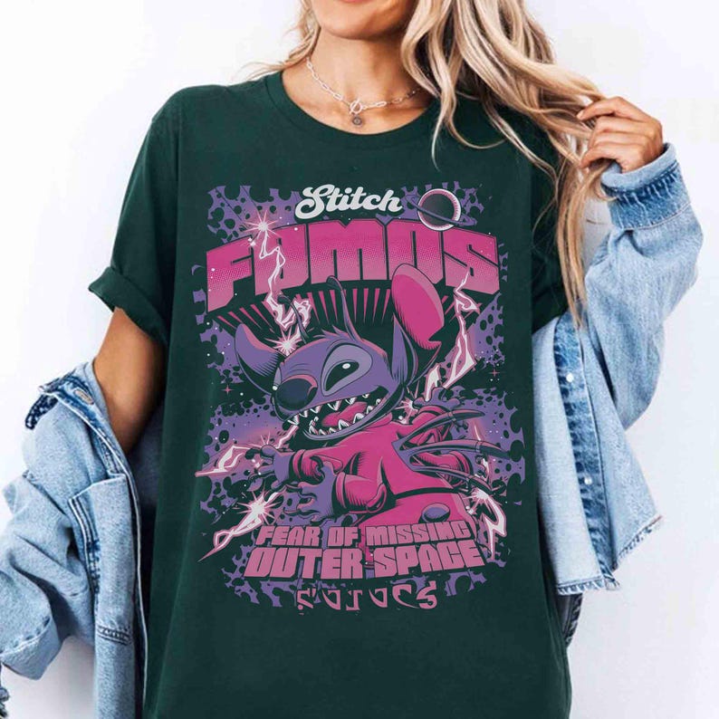 May include: Dark green t-shirt featuring Stitch from Lilo & Stitch. The graphic includes the words "Stitch FOMO" and "Fear of Missing Outer Space". Stitch is depicted in purple and pink with lightning bolts and a space theme.