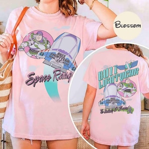 May include: A light pink t-shirt featuring a graphic of Buzz Lightyear and a spaceship with the text Space Ranger on the front, and a back graphic showing Buzz Lightyear, a spaceship, and the text Buzz Lightyear To Infinity & Beyond.