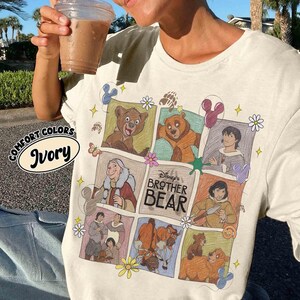 K&ouml;nnte beinhalten: Elfenbeinfarbenes T-Shirt mit einer farbenfrohen Grafik von Disneys B&auml;renbr&uuml;der. Das Design zeigt Cartoon-Bilder von B&auml;ren und Charakteren aus dem Film, mit dem Text "Disney's Brother Bear". Das Shirt hat auch die Worte "Comfort Colors" und "Ivory".