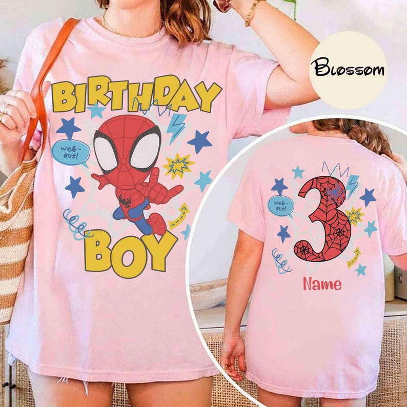 Pu&ograve; includere: Una t-shirt rosa chiaro con la grafica di un personaggio ragno, testo giallo BIRTHDAY BOY e stelle blu. Il retro della maglietta mostra un grande numero 3 con un motivo a ragnatela, stelle blu e la parola Name.