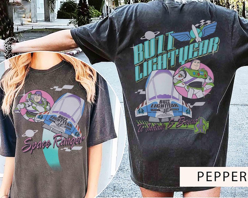 May include: A charcoal gray t-shirt featuring a graphic of Buzz Lightyear, a spaceship, and the text Buzz Lightyear, Space Ranger, and To Infinity & Beyond. The design includes a planet, wings, and a checkered flag pattern in teal, purple, and white.