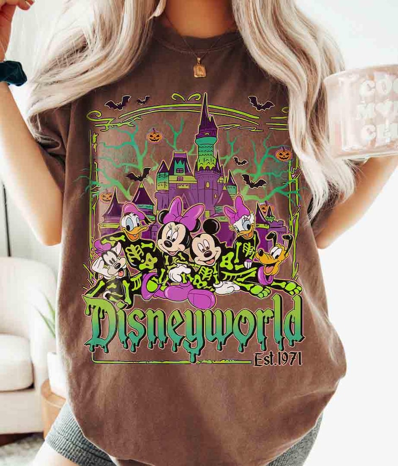 May include: Brown t-shirt with a Disney World Halloween design. The graphic shows cartoon characters, a castle, bats, and pumpkins. The words "Disneyworld" are in green and purple, with "Est. 1971" underneath.