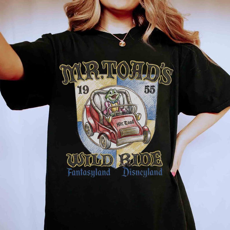 K&ouml;nnte beinhalten: Schwarzes T-Shirt mit einem Aufdruck von Mr. Toad's Wild Ride aus Disneyland. Das Design zeigt ein rotes Auto mit Mr. Toad, den Text "Mr. Toad's Wild Ride" und die Jahreszahlen 19 und 55. Das Shirt ist ein klassischer Stil.