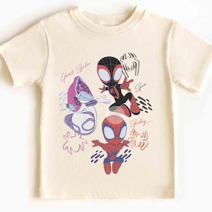 Op de afbeelding: Cr&egrave;mekleurig T-shirt met cartoon illustraties van Spider-Man personages. Het shirt toont Ghost Spider, Spin en Spidey, met hun namen in cursief. Het ontwerp gebruikt rood, zwart, blauw en paars.